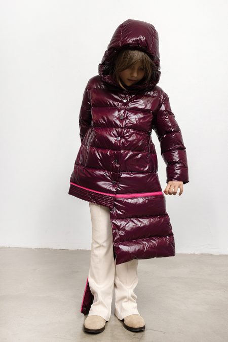 Girl in winter coat in burgundy colour, with pink zipper and hood, detaching the lower panel of the coat