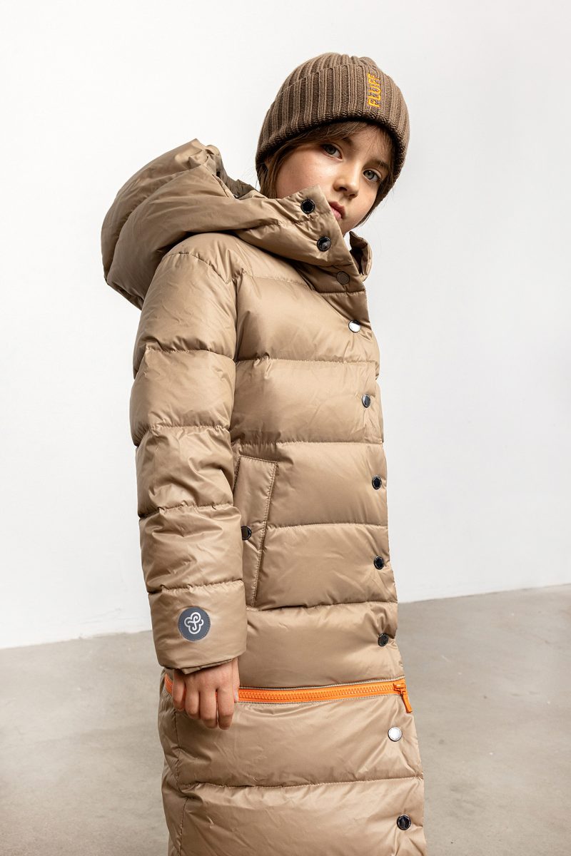 Girl in winter coat in beige colour, with orange zipper and hood, side photo