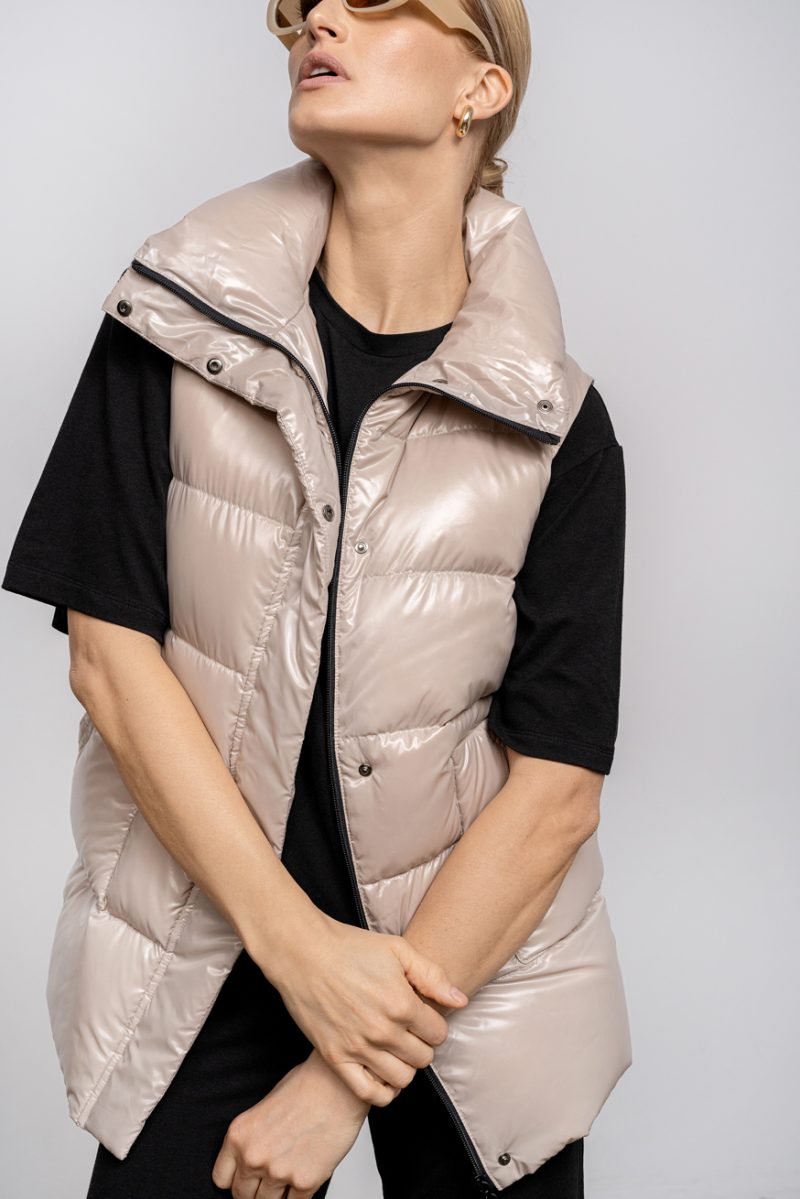 Beige vest with high collar and two front pockets. Zipper and stud fastening. Vest with an elastic waistband on the back and natural goose down filling.