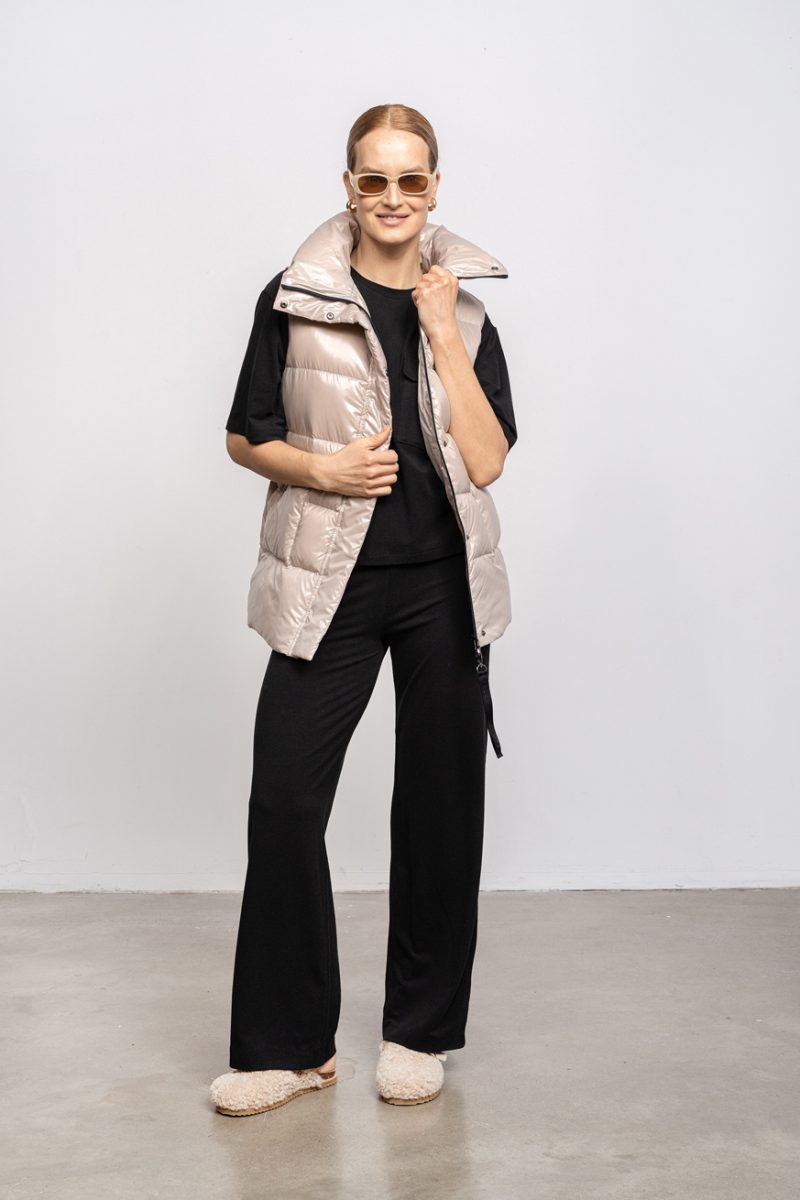 Beige vest with high collar and two front pockets. Zipper and stud fastening. Vest with an elastic waistband on the back and natural goose down filling.